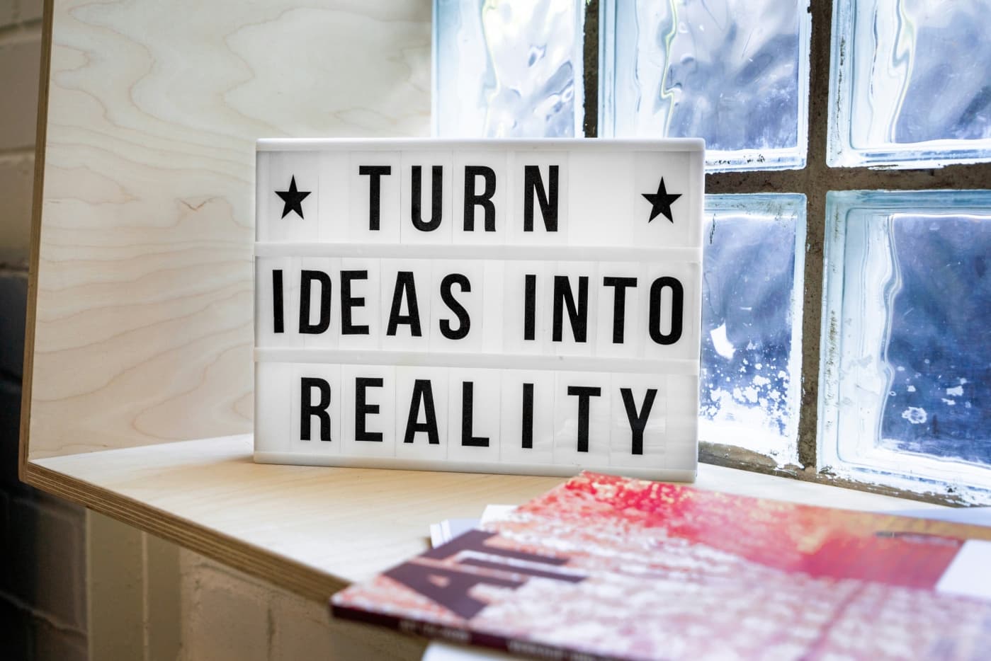 Reader board/marquee letter sign with the words 'Turn Ideas Into Reality' on a shelf in front of a pane glass window.